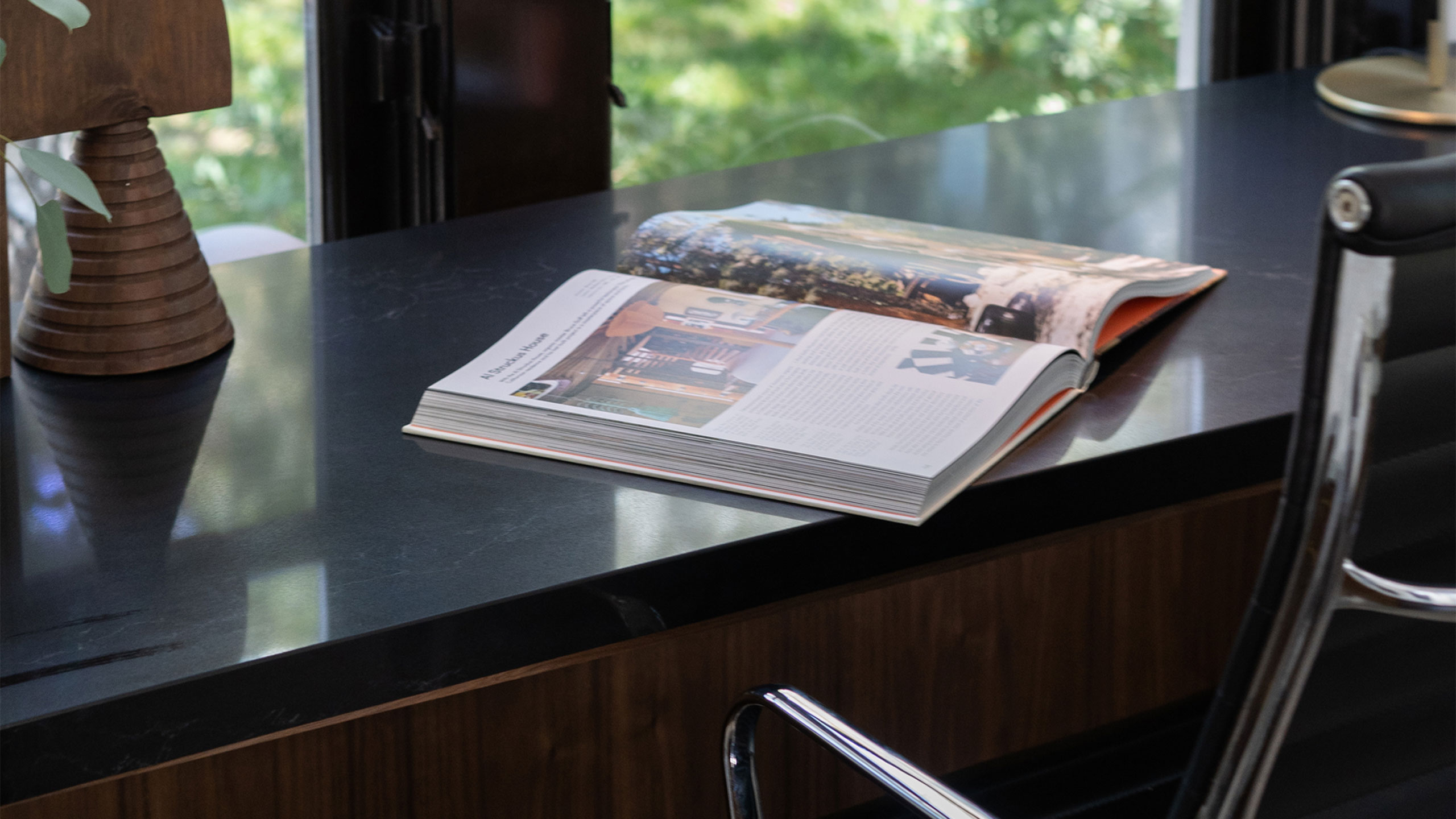 An office chair is sitting at a desk with a black quartz countertop and an open book sitting on top.