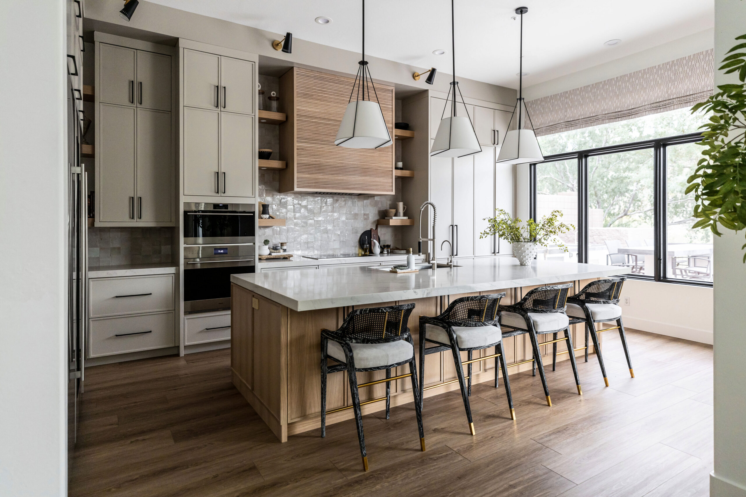 This kitchen features tall cabinets and hanging light fixtures. There’s a big kitchen island with four bar stools sitting around it.