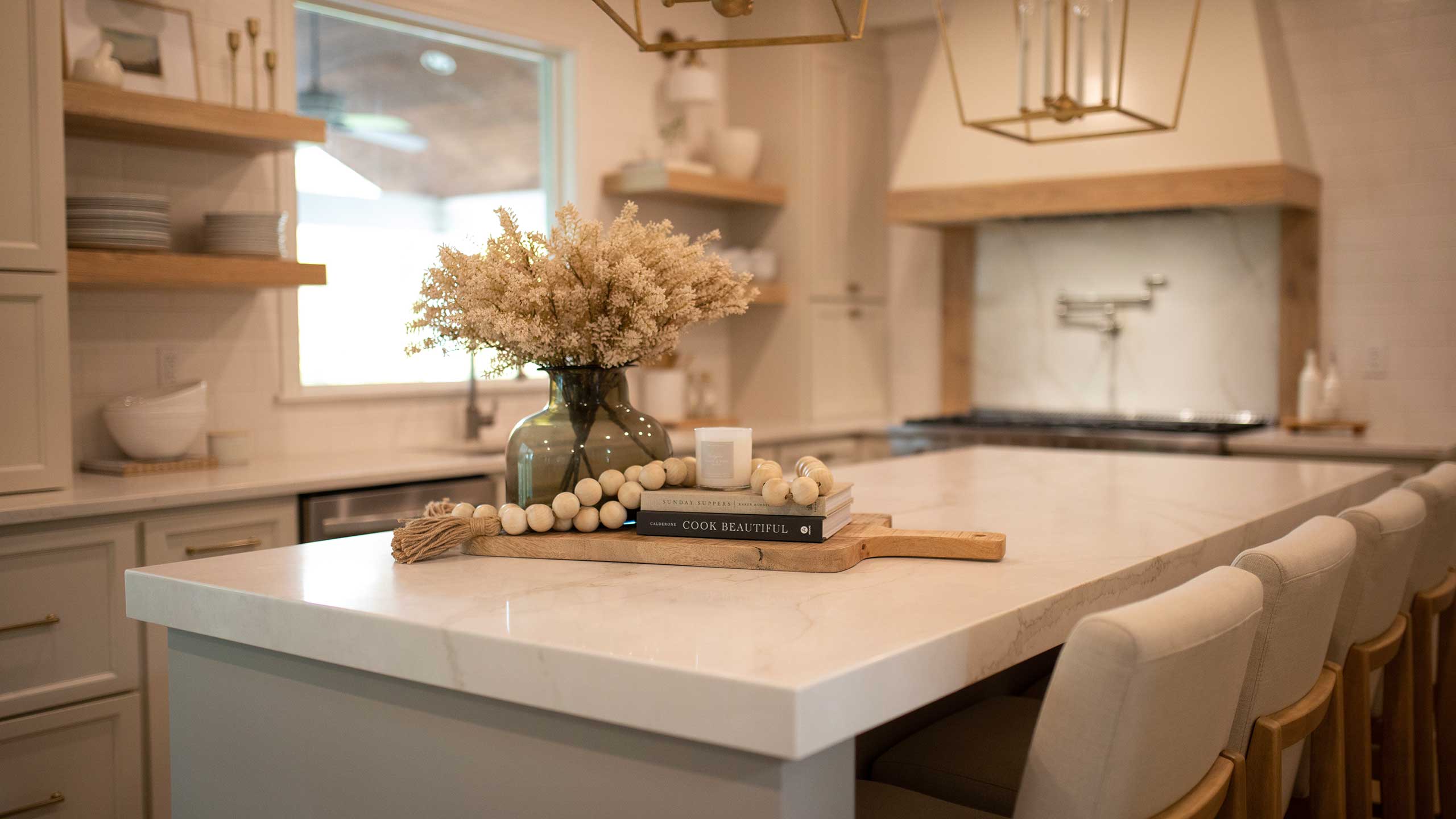 This kitchen features white cabinetry and an island with a white quartz countertop. There is decor sitting on the island.