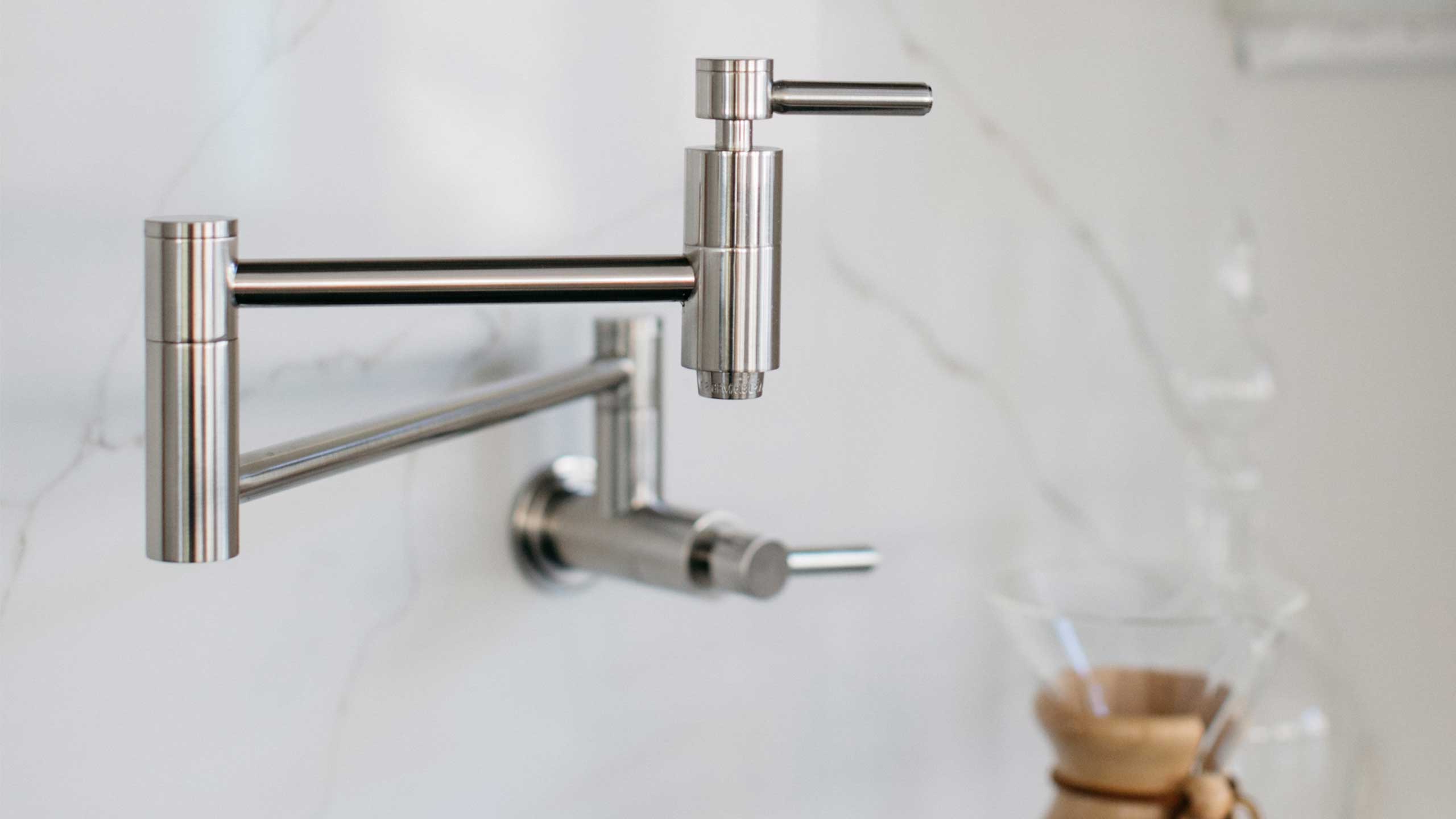 A white quartz backsplash with a mounted pot filler faucet is pictured