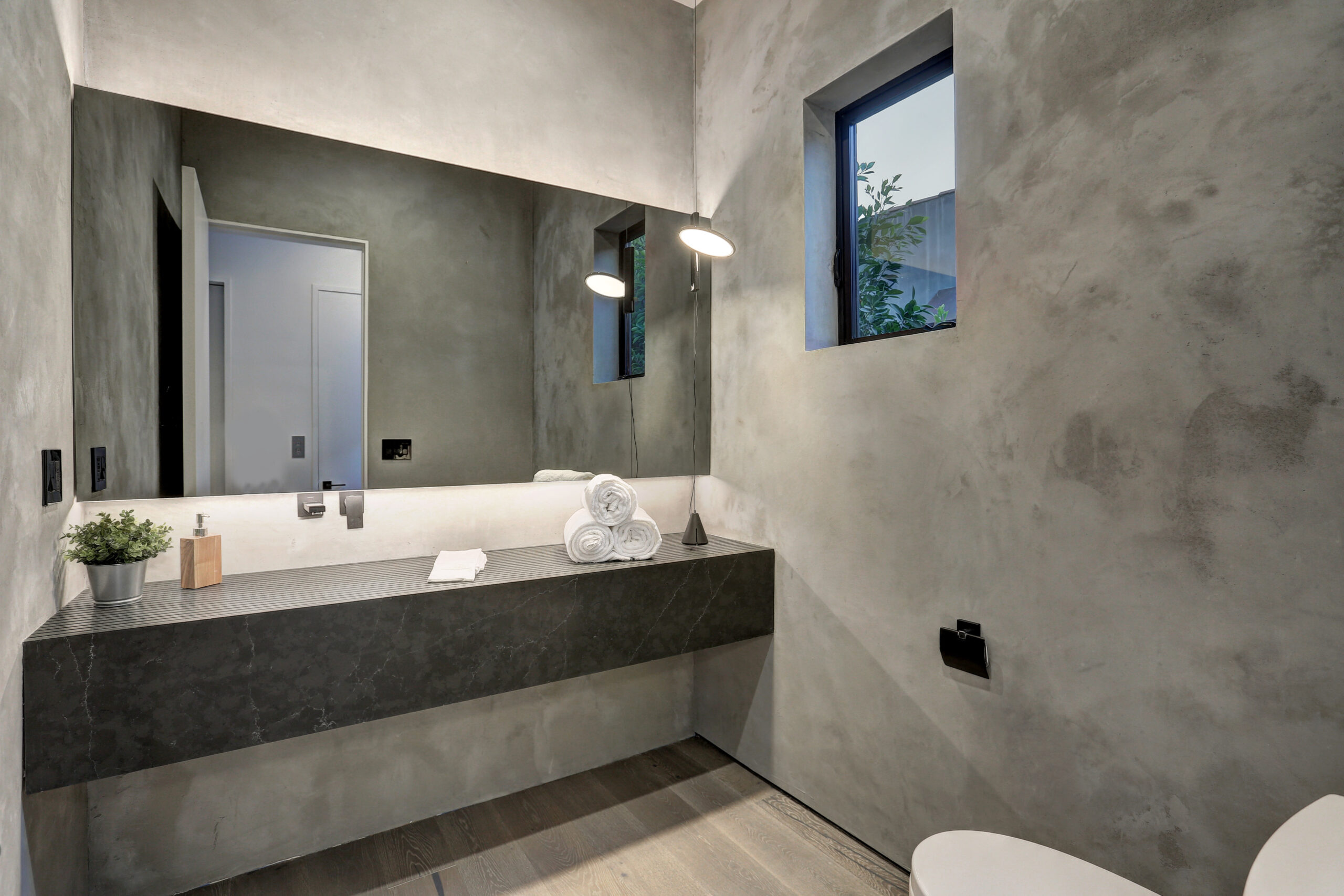 This gray bathroom has a thick black quartz countertop with towels sitting on the counter and a mirror in the background.