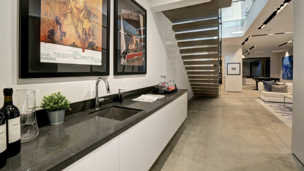 This bar area features white cabinets and a black quartz countertop. There are two movie posters framed above the bar.